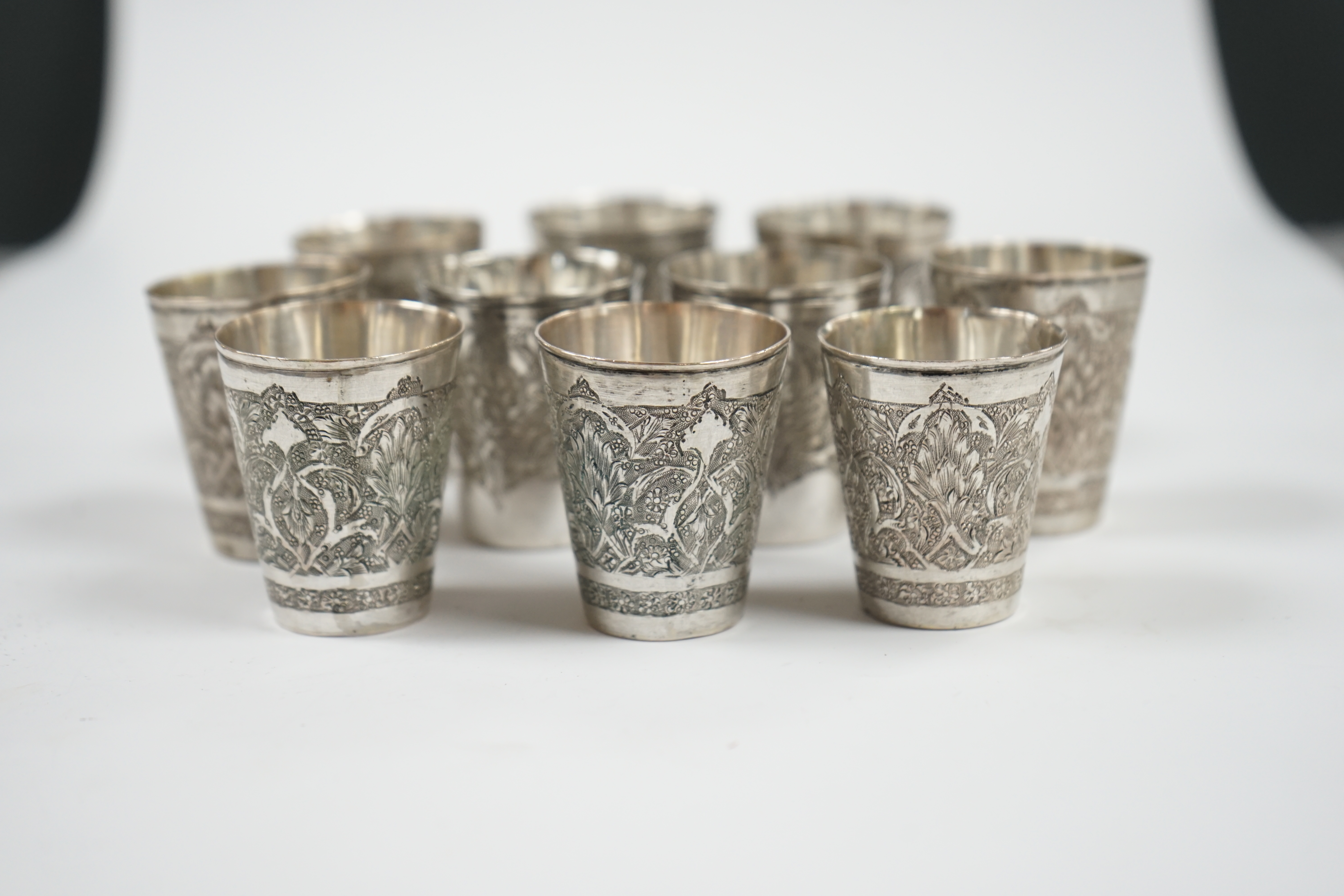 A set of four Persian engraved white metal tot cups, 43mm, stamped marks to the base and six other similar tot cups, 44mm, 8.7oz. Condition - fair